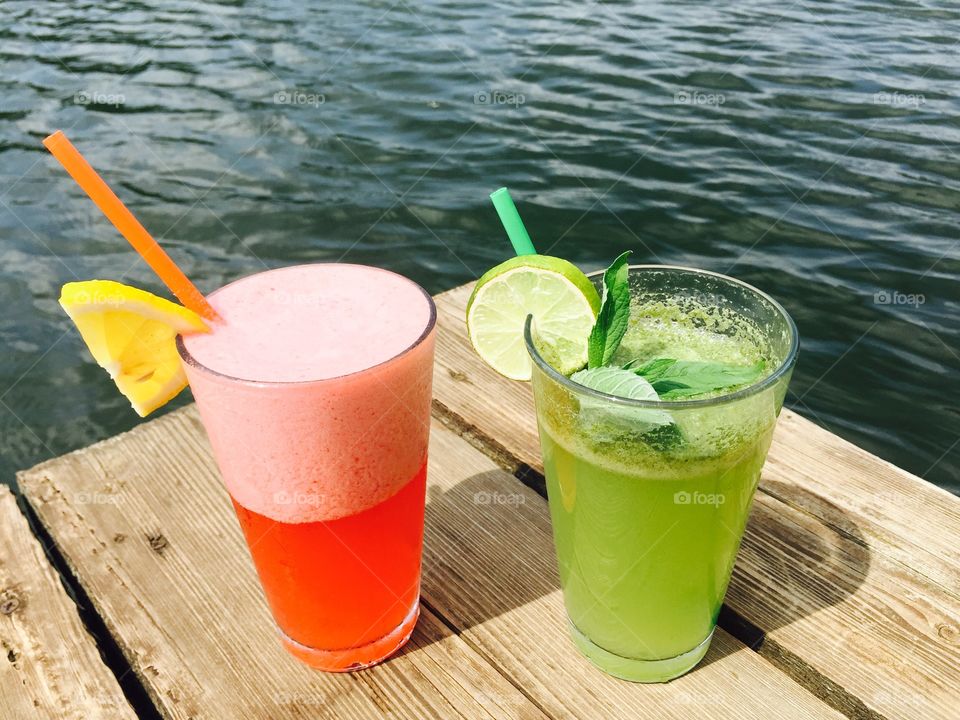 Strawberry lemonade and mint lemonade glasses near the lake