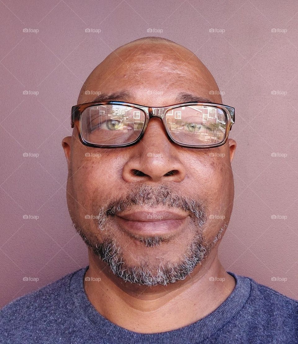 Portrait of a man with a bald head and a Gray beard wearing Brown reading glasses