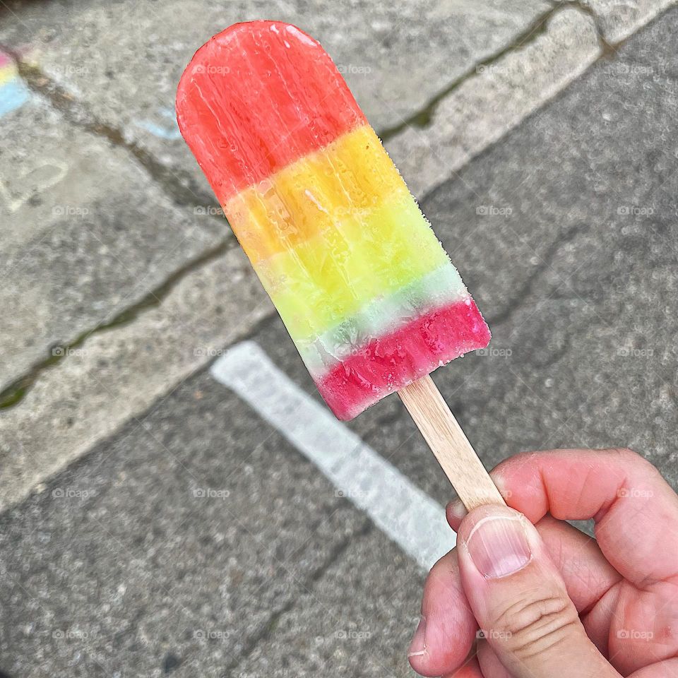 Eating a Pride Popsicle at Pride Event, rainbow colored popsicles, woman’s hand holding rainbow Popsicle, hand holding popsicle at Pride parade, the colors of pride 