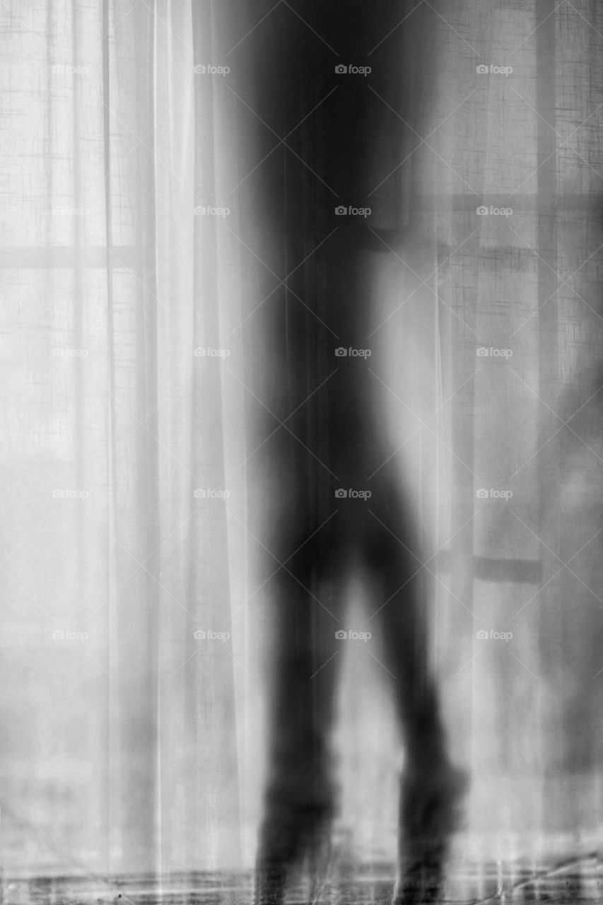 Artistic black and white photo of the shadowy legs of a woman dancing ballet in front of a curtain