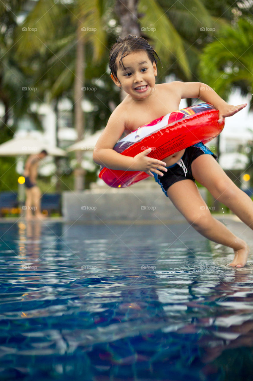 young happy boy ready to jump in the pool at a resort on a hot sunny summer day