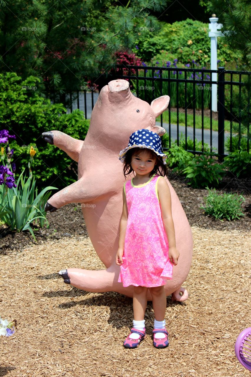 Adorable little girl in pink posing on sunny day in Garden with pig statute