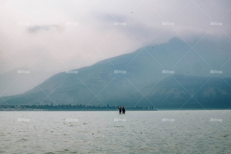 standing in the middle of a baby blue lake in Alberta Canada with smoky mountains in the background