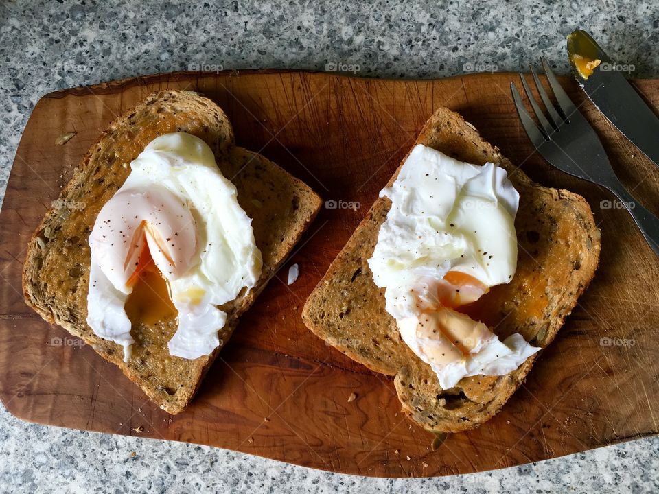 Poached eggs on toast on olive wood with cutlery 
