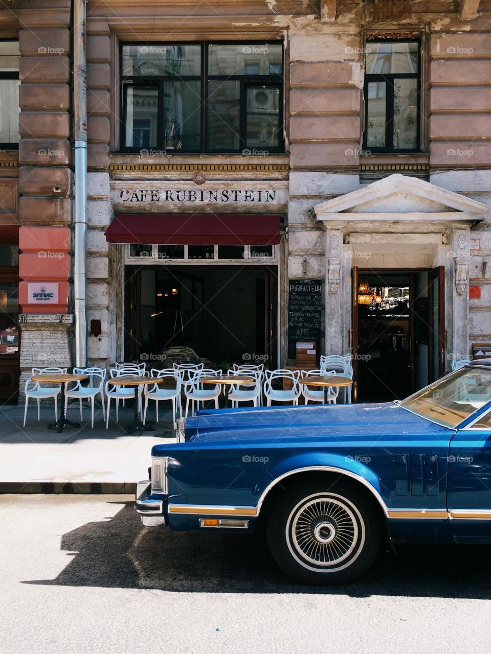 A blue retro car stands outside an outdoor cafe on a sunny summer day, nobody 