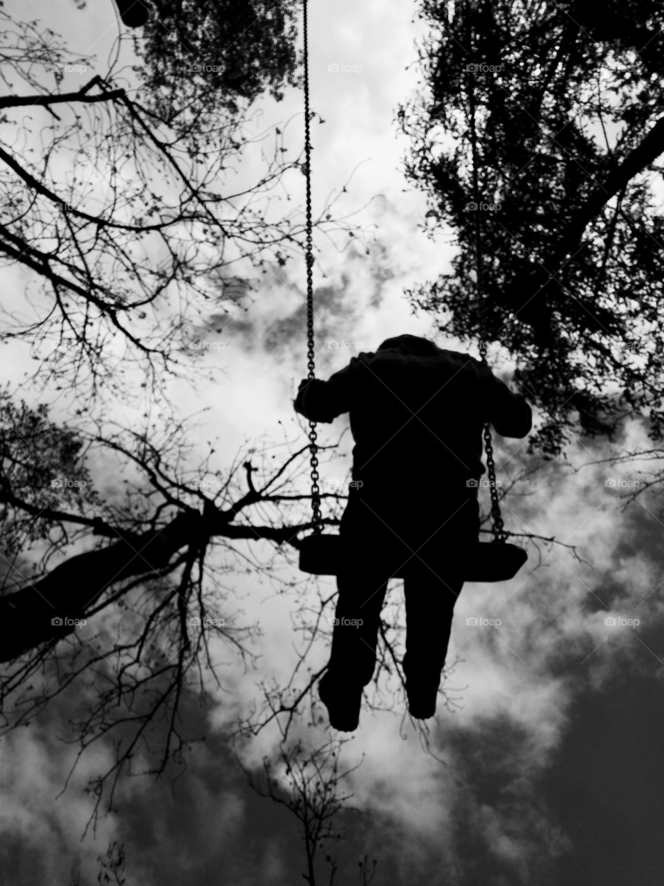 Boy of 8 years is on the swing. Low angle. Black and white