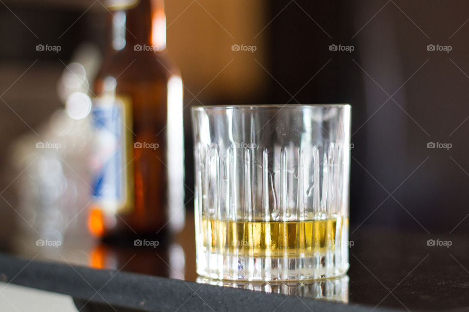 A glass with a small amount of a drink resting on a bar