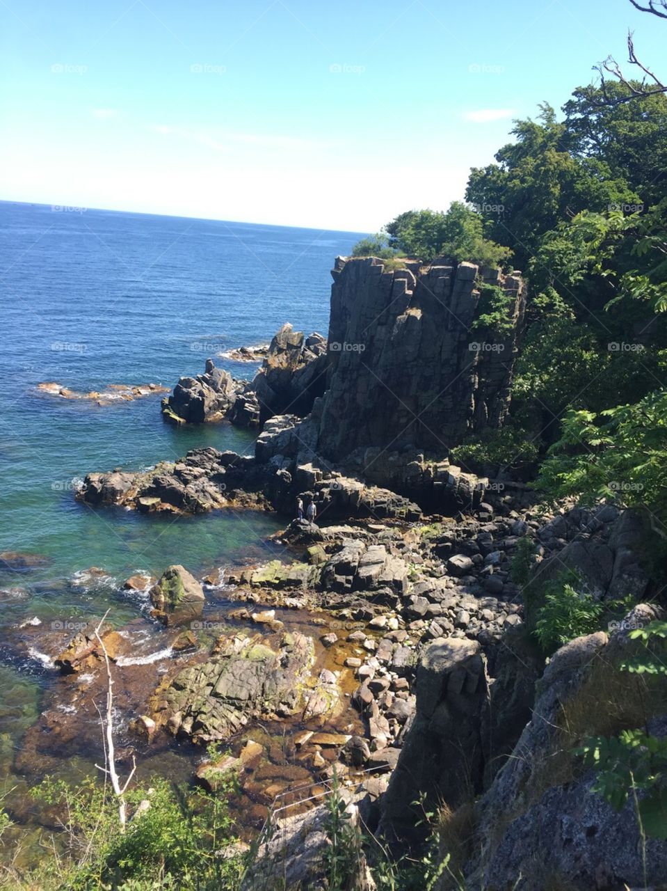 Rocky shore overlooking the blue, Baltic Sea off the island of Bornholm. Cliffs with trees tower over the beach. 