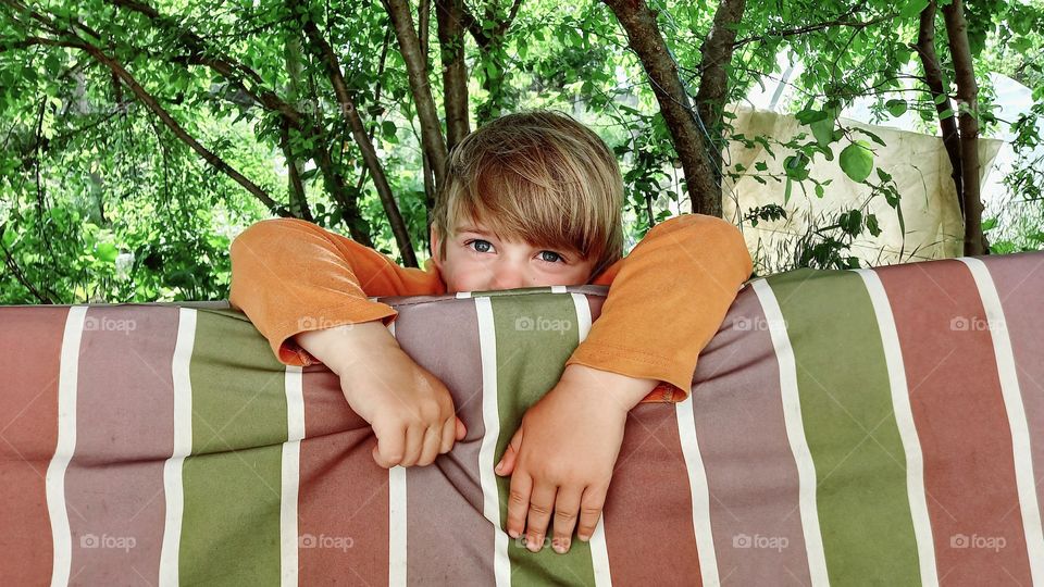 a little boy peeking out from behind a chair