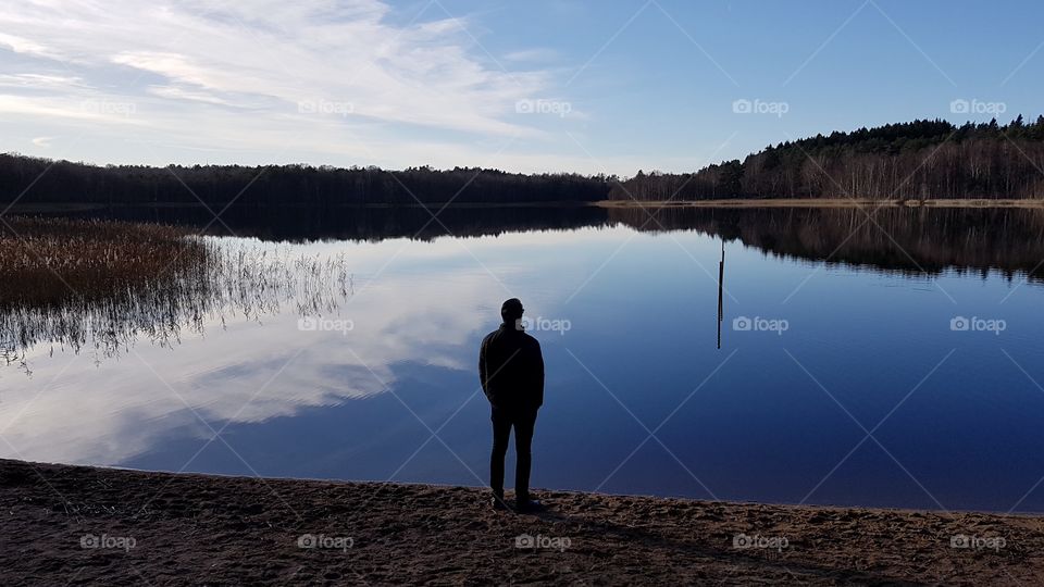 Man standing on the beach looks over mirrored lake - man står på stranden, tittar ut över spegelblank sjö