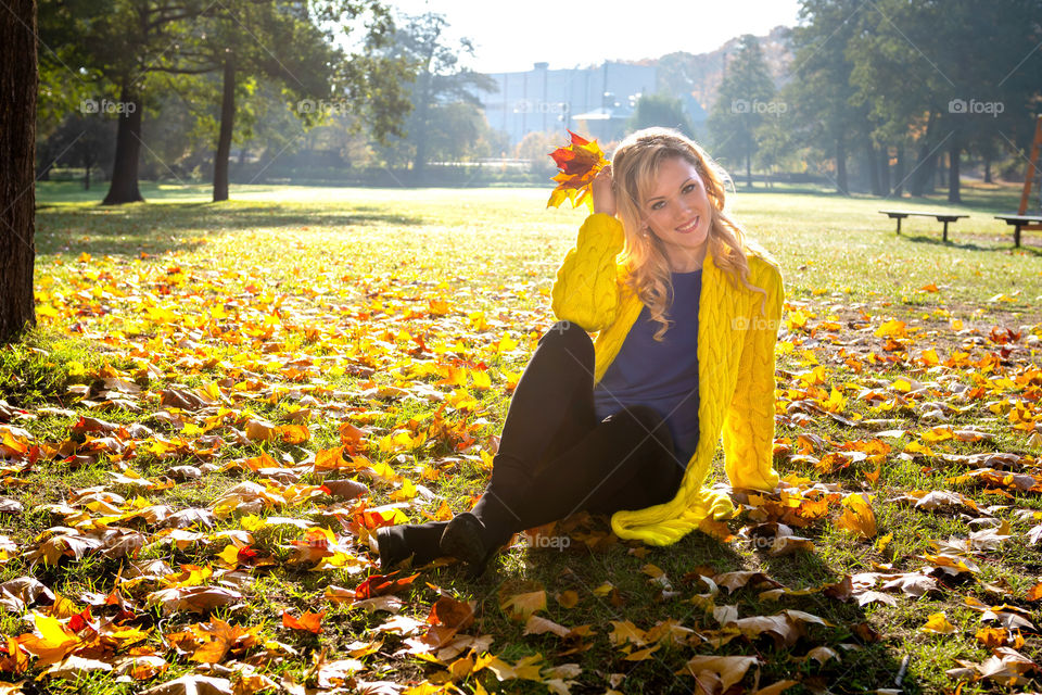 A young, beautiful, blonde woman walking through the autumn park and rejoice in colorful tree leaves.
