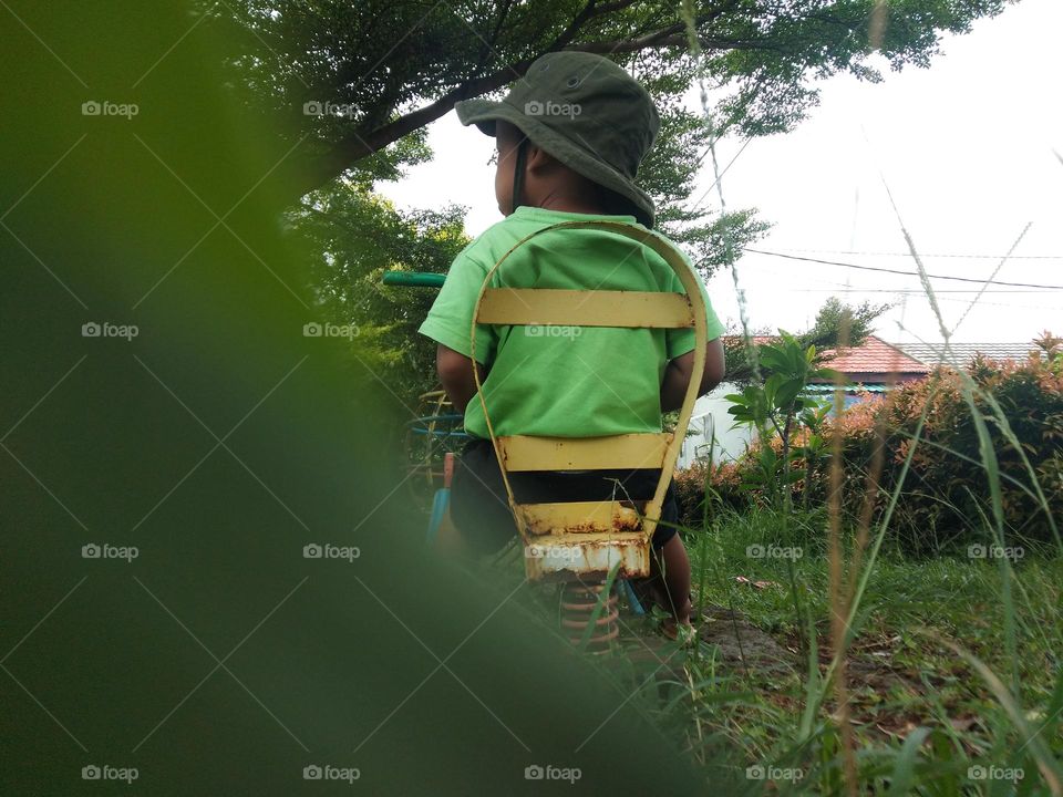 a boy playing alone in play ground use green cloth and hat