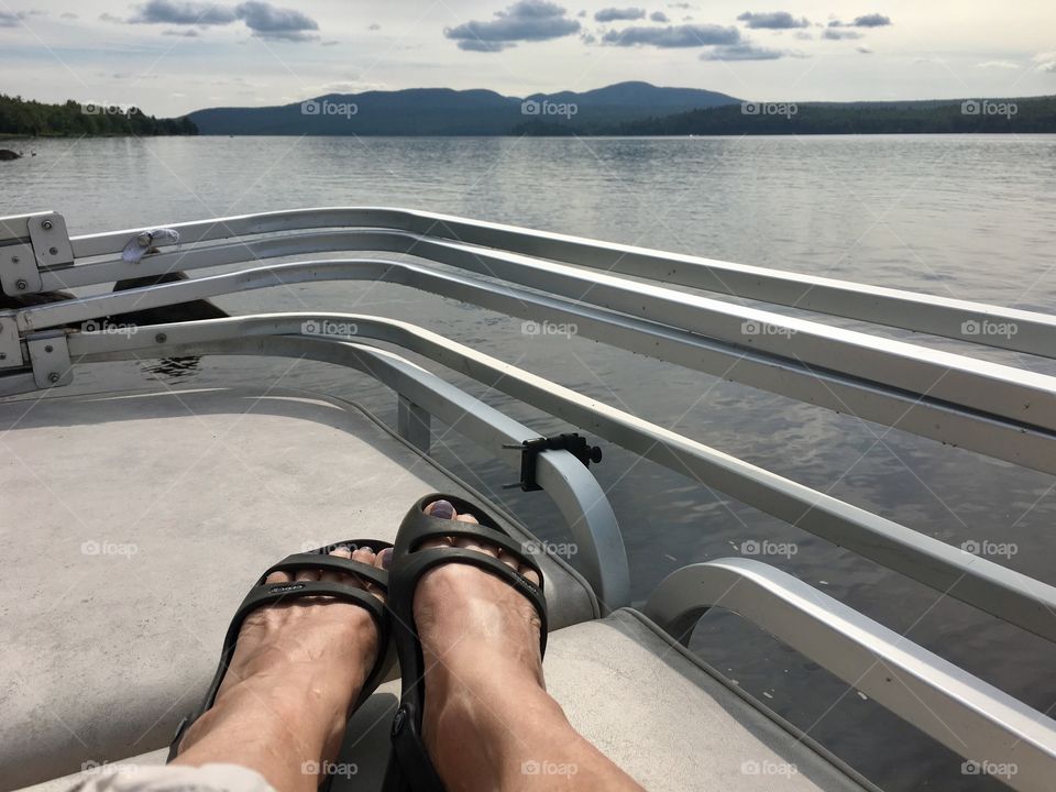 A lazy day on flat bottomed boat on Chateaugay Lake in the Adirondack mountains of New York State; female feet in sandals; point of view