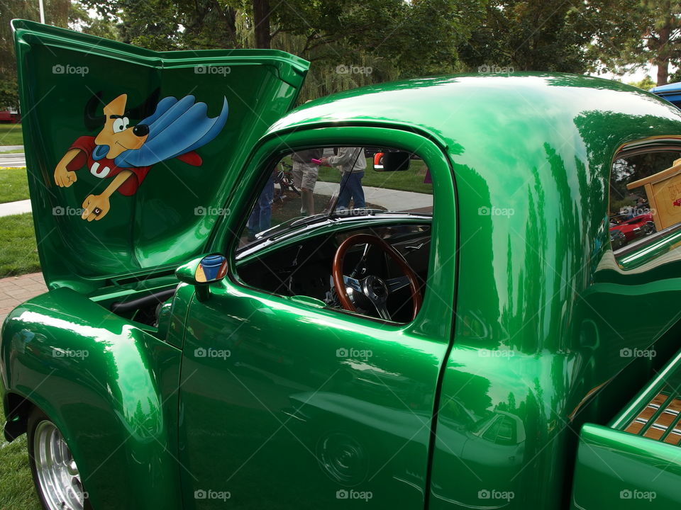 An Underdog cartoon character painted on the inside of a raised hood on a classic bright apple green pickup at the annual car show in Drake Park in Central Oregon during the summer. 
