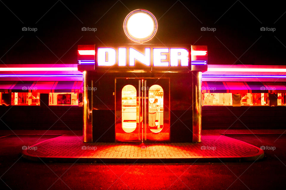 The doorway and entrance to a traditional American diner with brightly coloured neon lights fluorescent colours at night