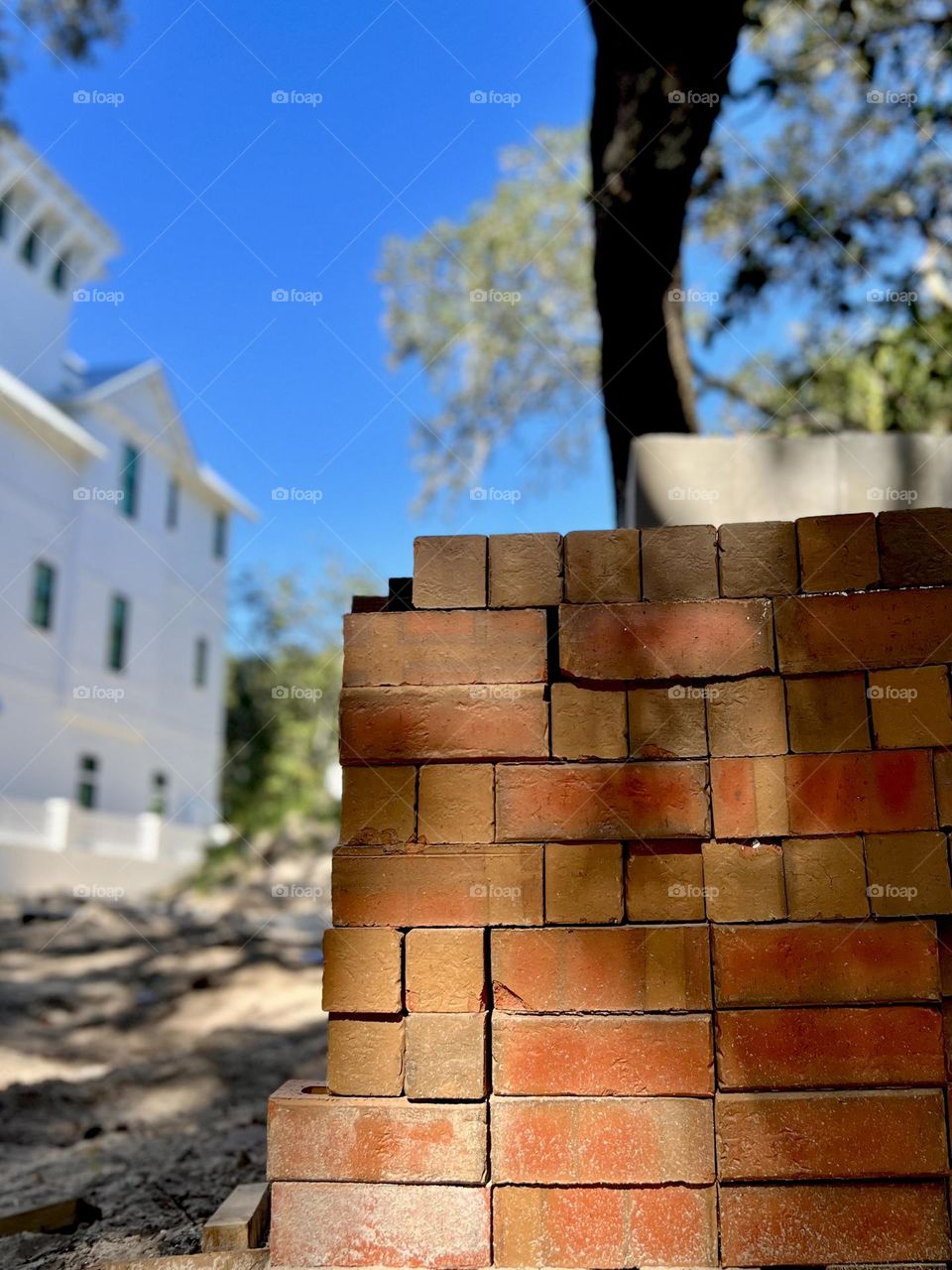 Foreground focus on a stack of red masonry bricks. Tree, blue sky and house are in background.