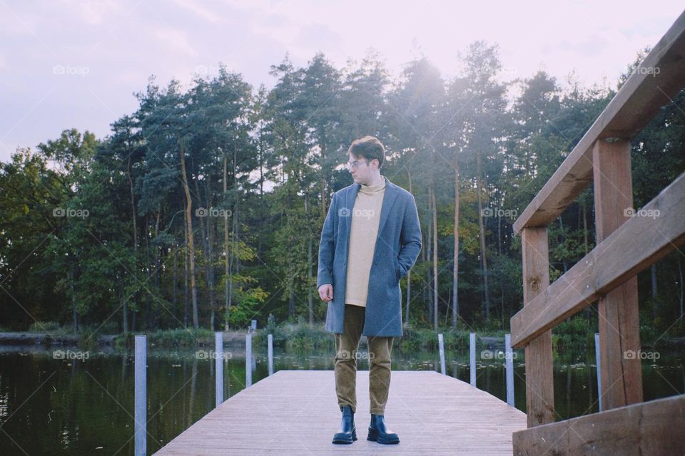 A young man standing on a bridge against the background of a lake