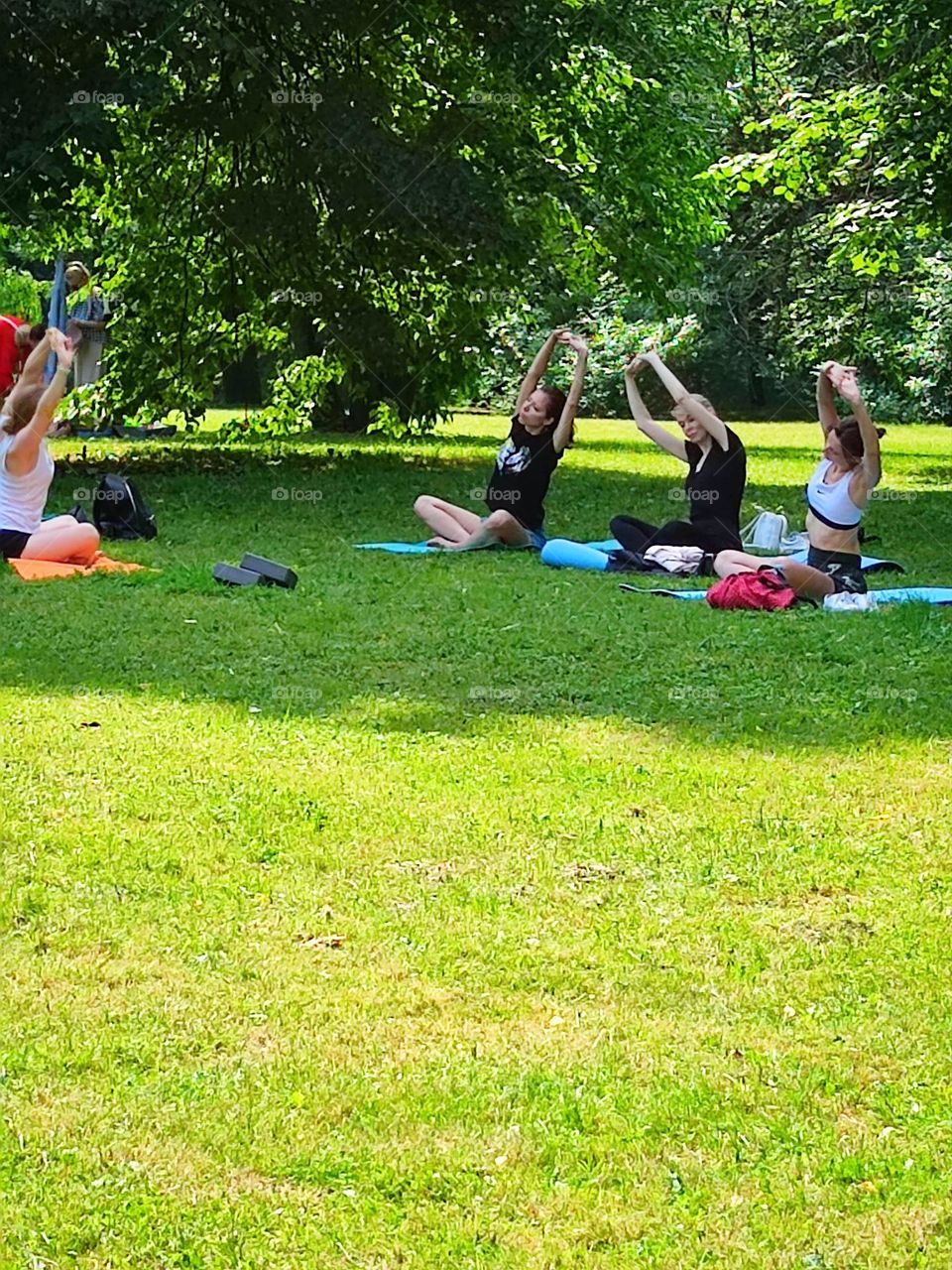 Summer day.  Time to bring your body back to normal in the fresh air.  Three young girls are sitting on a green meadow and doing yoga.  The instructor shows the correct poses