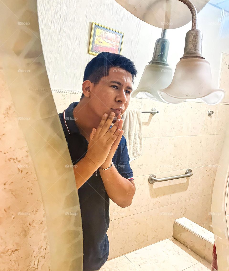dark-skinned man observing the skin of his face in the bathroom mirror, touching his chin with his two hands