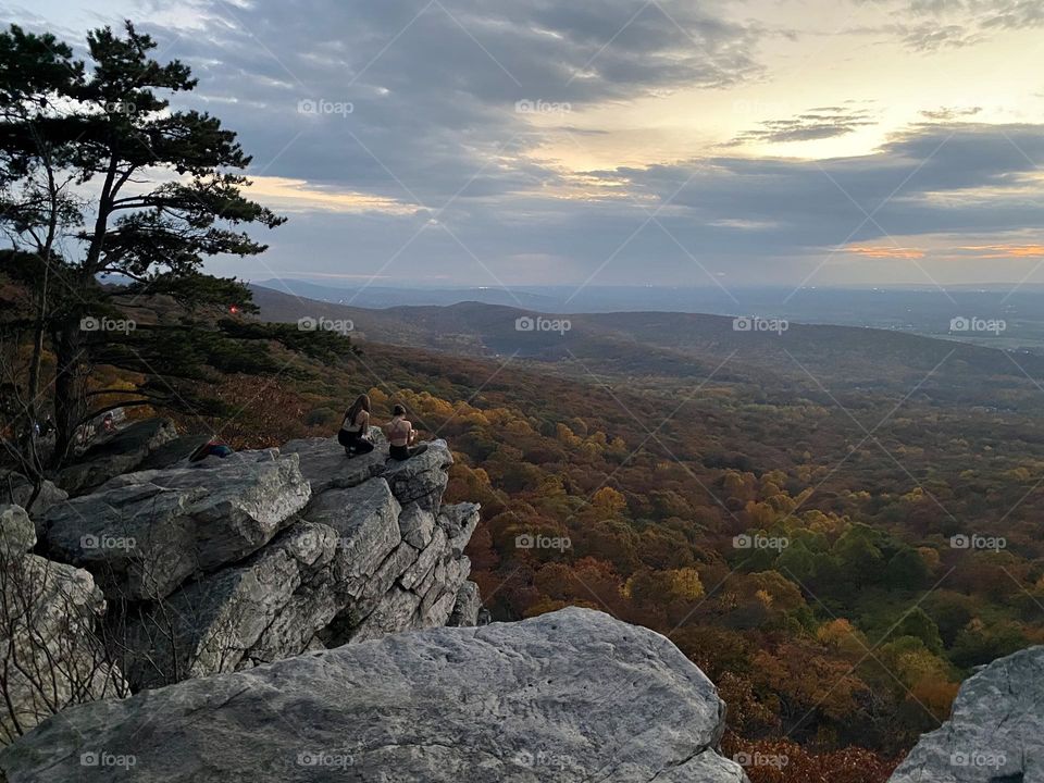 Two people sitting on rocks at a scenic overlook as the sun sets