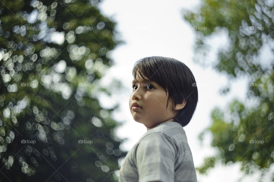 outdoor portrait of happy young eurasian boy on a blurry out of focus bokeh foliage background