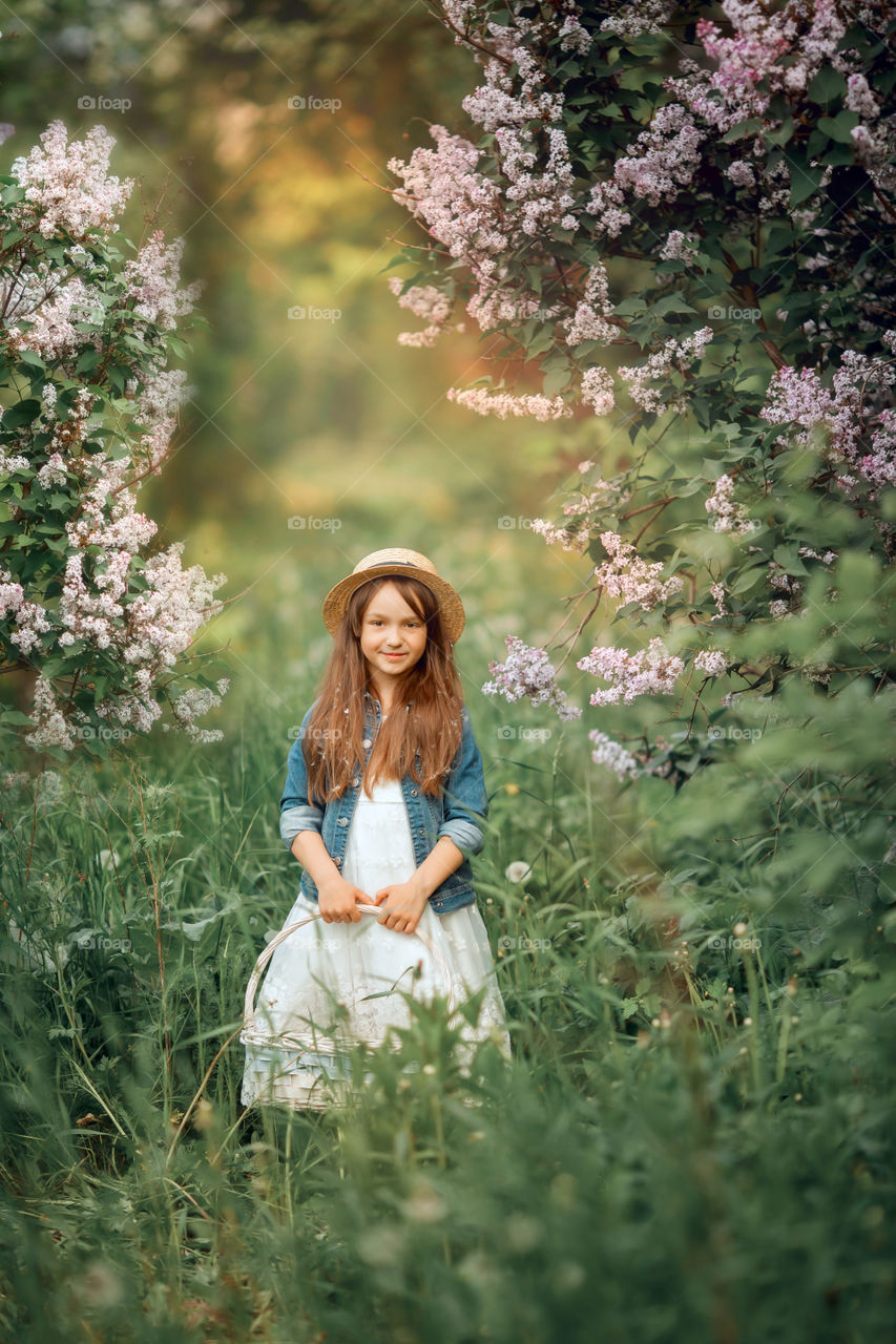 Little girl in a hat near blossom lilac tree at sunset 