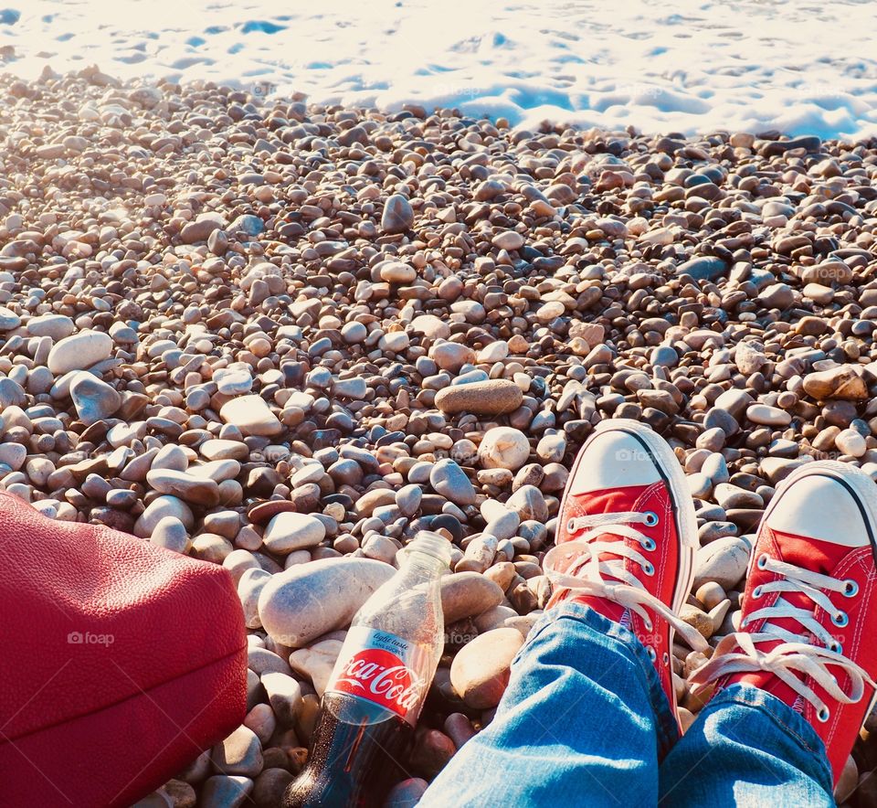 A bottle of Diet Coke on the beach with red sneakers.