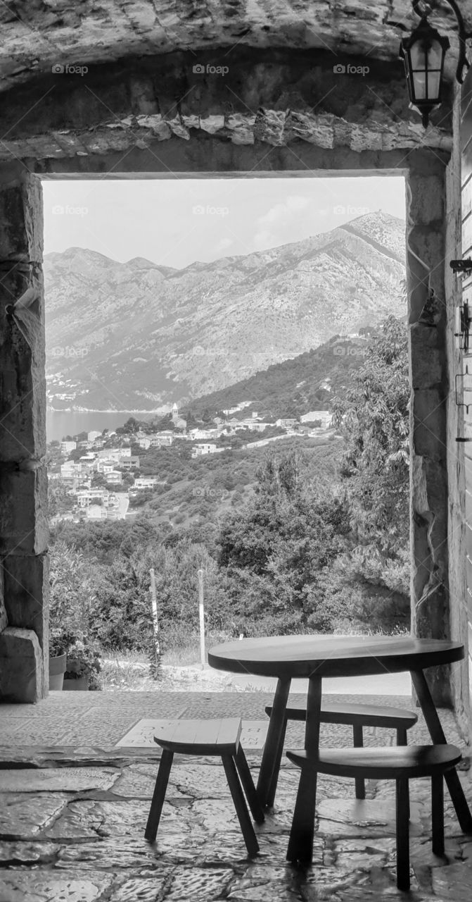Wooden table and chairs in an outdoor cafe in the old Dolmatian city with stone walls and picturesque summer views of the small old coastal town, olive gardens, sea and mountains. Summer holidays in the old European Mediterranean town