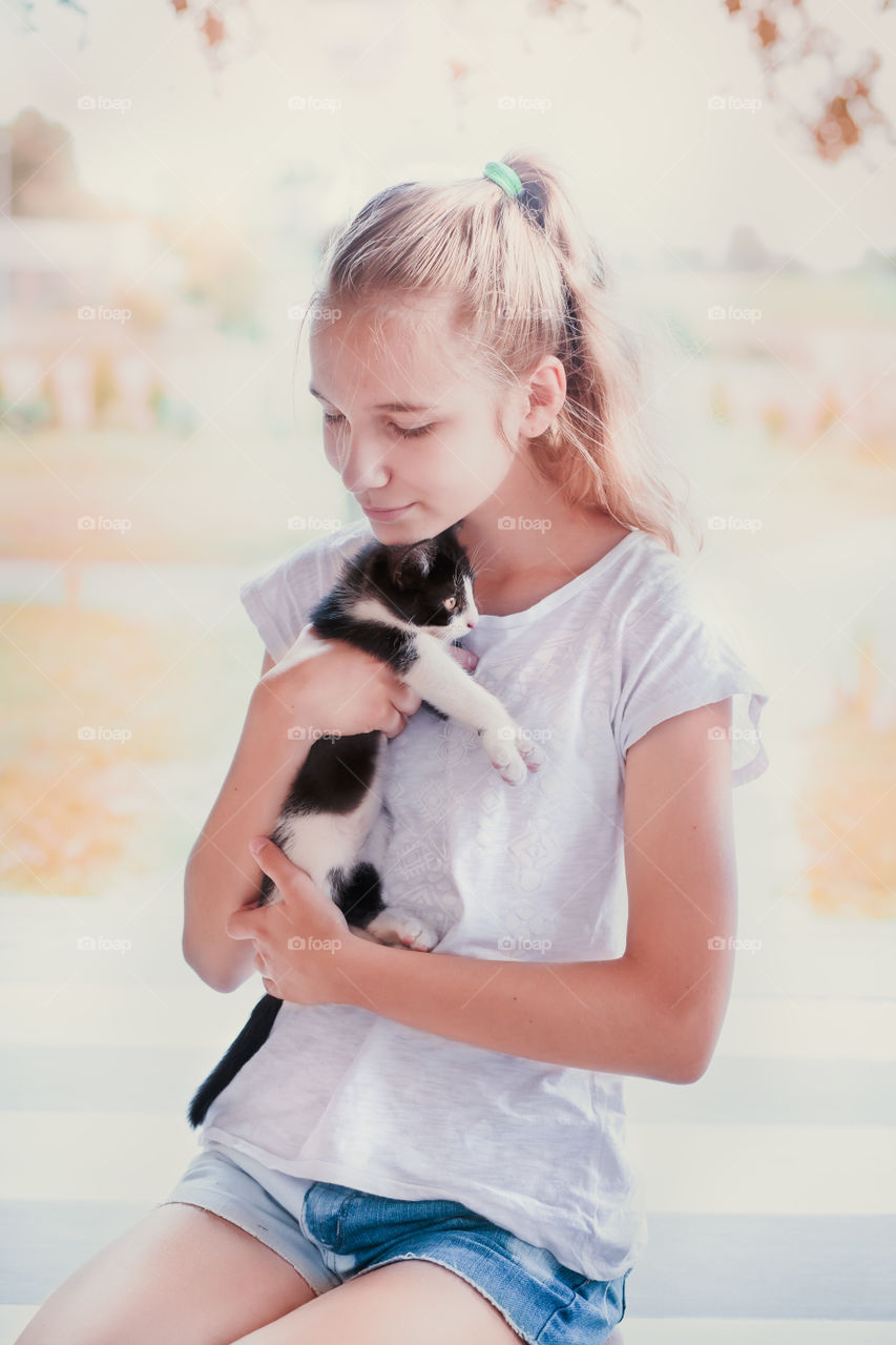Young beautiful girl squatting on the porch and hugging her little cat