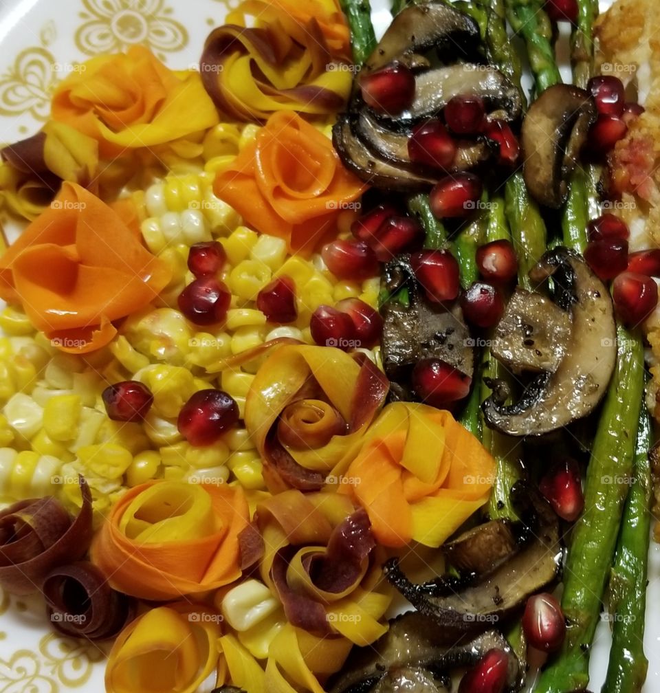 Autumn harvest vegetable plate. Freshly cut corn, multi-colored yellow, orange and purple carrot strips, steamed and folded into flowers, and served with asparagus and mushrooms. Drizzled with melted butter and sprinkled with pomegranate arils.