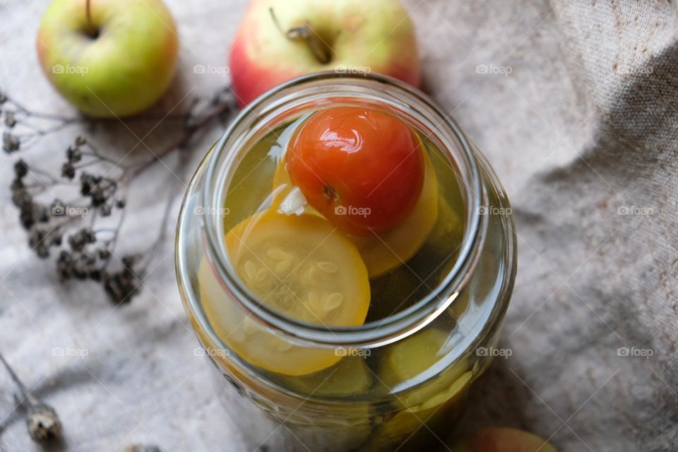 Opened glass jar with pickled vegetables close-up and apples on the background