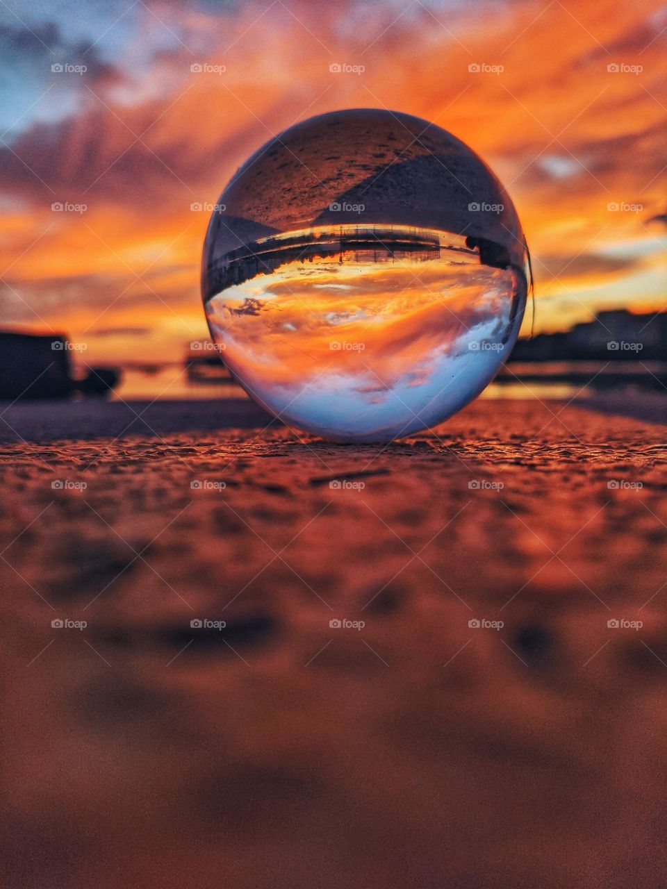 Top view of lensball, crystal ball on the beach, seashore close up. Reflection of beautiful red sunset sky in lens ball. Abstract