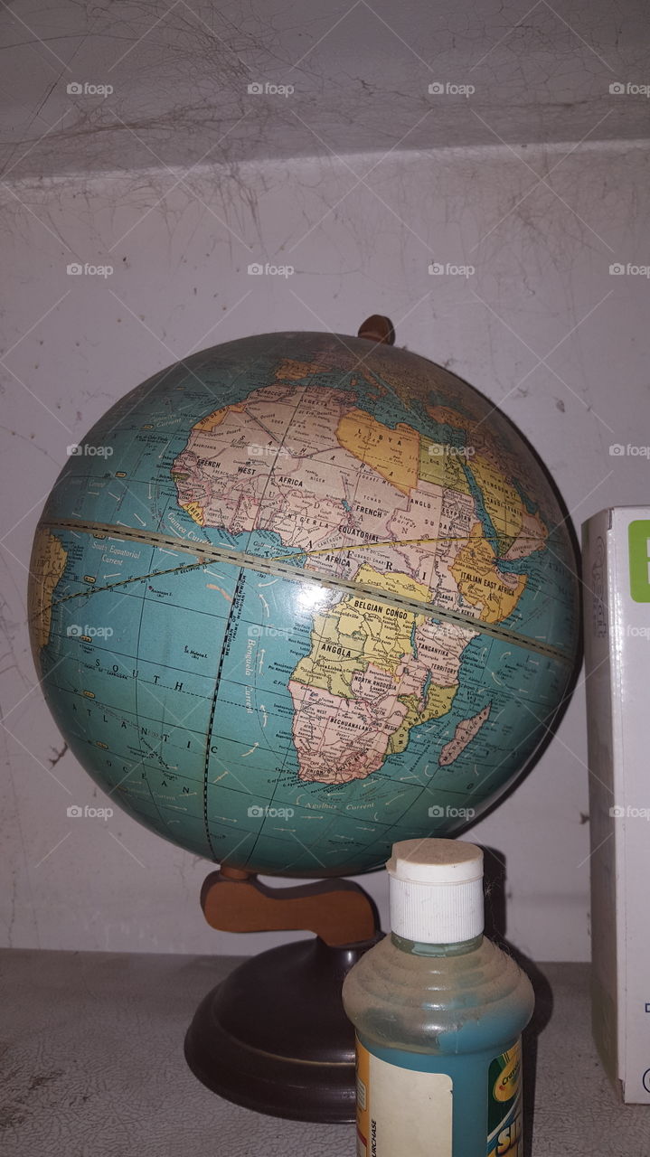 A round globe that is featuring the continent of Africa sitting on top of our refrigerator. In front of the globe is some blue paint.
