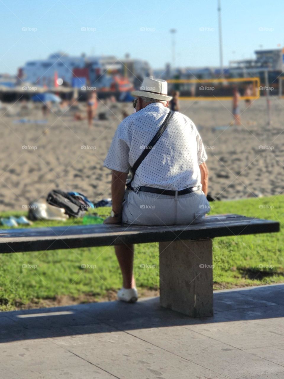 old man with a hat sitting on a bench on the beach - very relaxed break