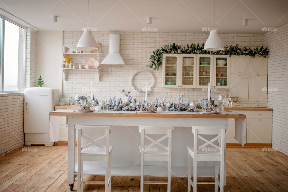 Festive winter cozy kitchen interior with garlands, decorations and gifts.  Christmas dinner at the decorated table.