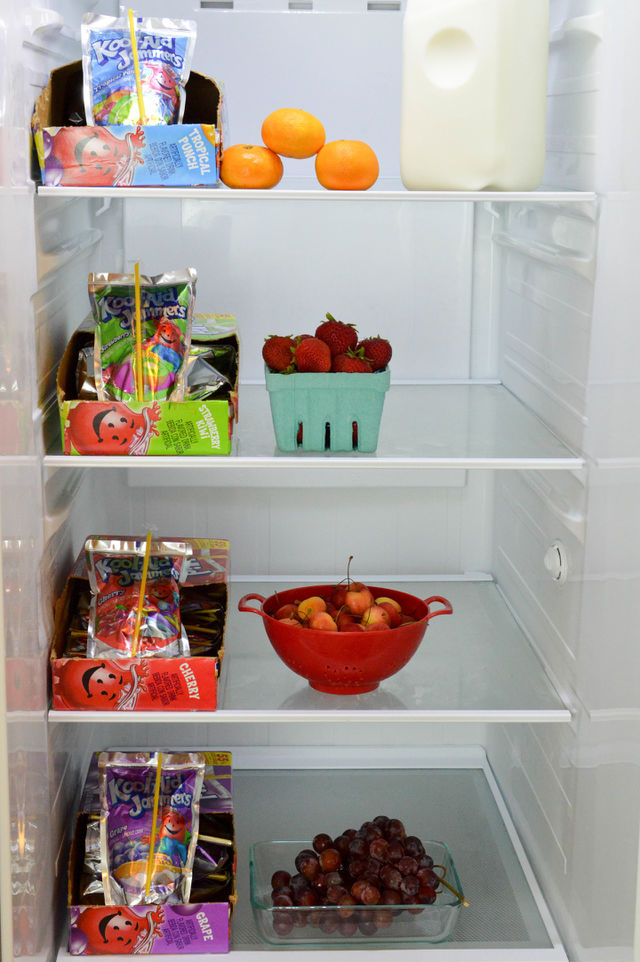 Drink pouch cases of assorted flavors shown in an open refrigerator with fruit