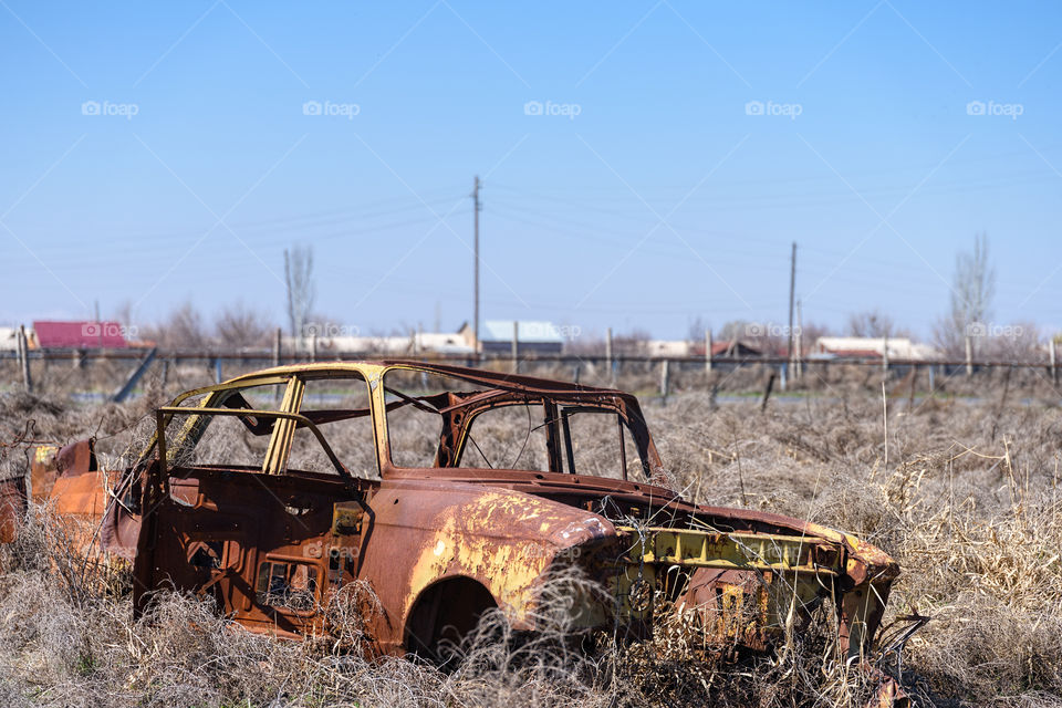 Abandoned and rusty wreckage of an yellow vintage Soviet Russian car in the middle of dry hay with scenic ice top mountains and clear blue sky on the background in rural Southern Armenia in Ararat province on 4 April 2017.