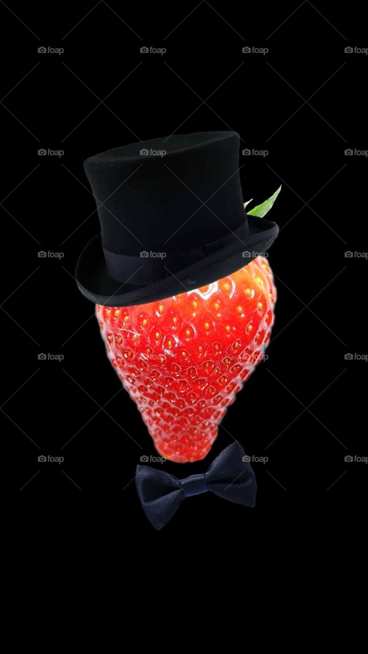 Fruit.  Red strawberries in a black top hat and black bow tie.  Black background. Mister strawberry