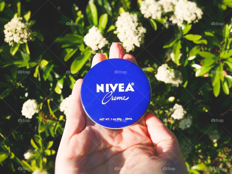 Nivia Cream in a Woman's Hand with Flowers Outside