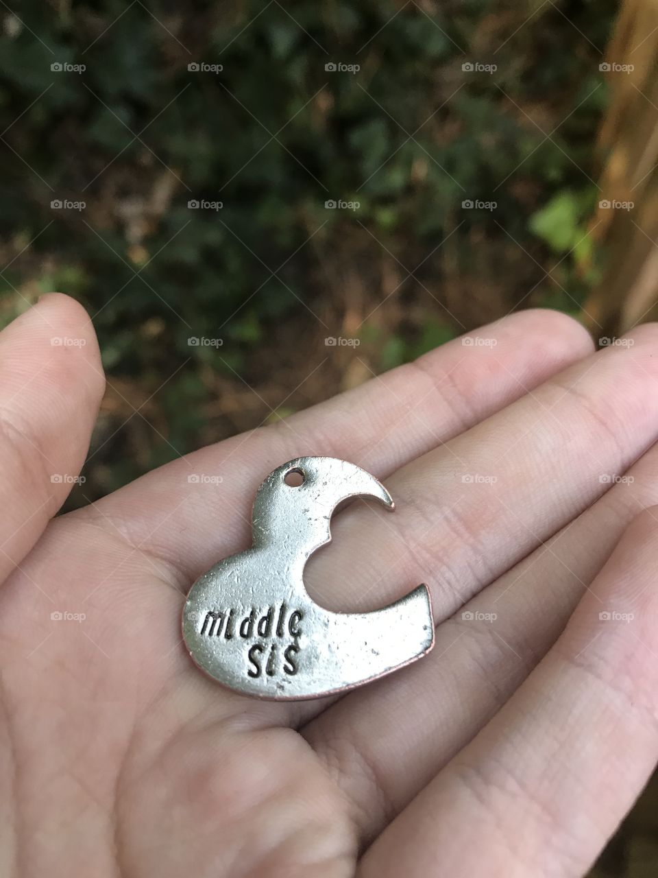 A person outside holding a heart-shaped silver charm reading “Middle Sis”