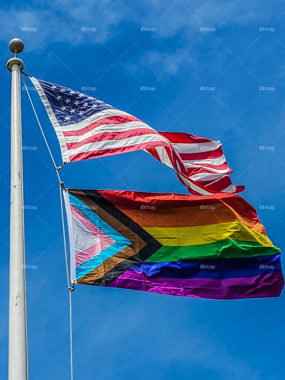 The Gay Pride Flag flying proudly in the sky with the American flag flapping in the wind for pride month 