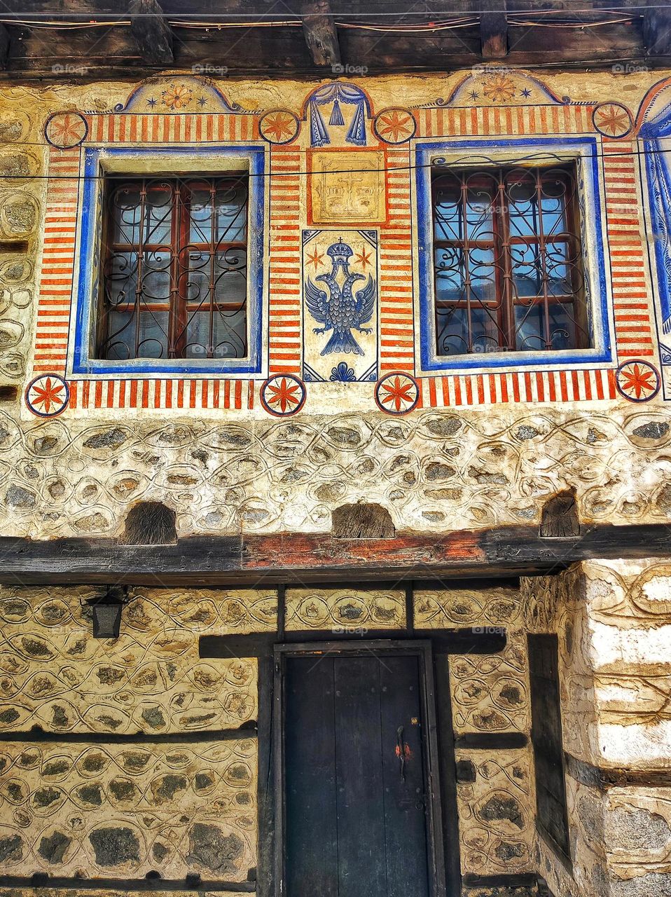 A photo of an old Bulgarian house made with wood and stone, with an intricate design above the entrance