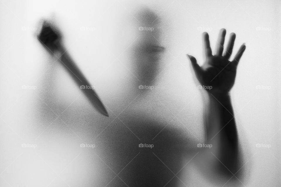 Horror Murderer. Dangerous man behind the frosted glass with a knife on his hand.Halloween background.Black and white picture