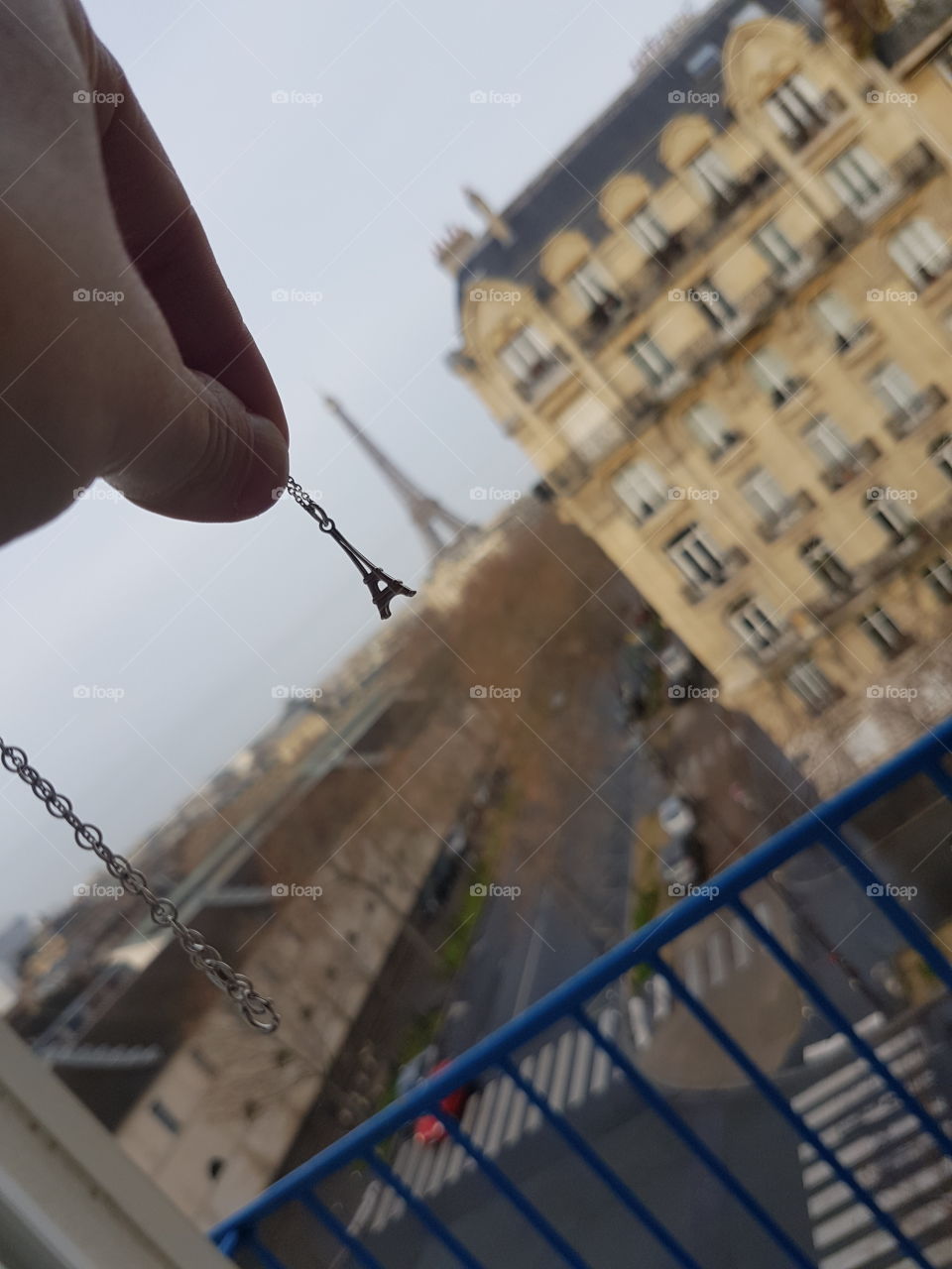 Seeing double, hand holding an eiffel tower necklace charm up to a distant real eiffel tower in Paris, France, same shape.