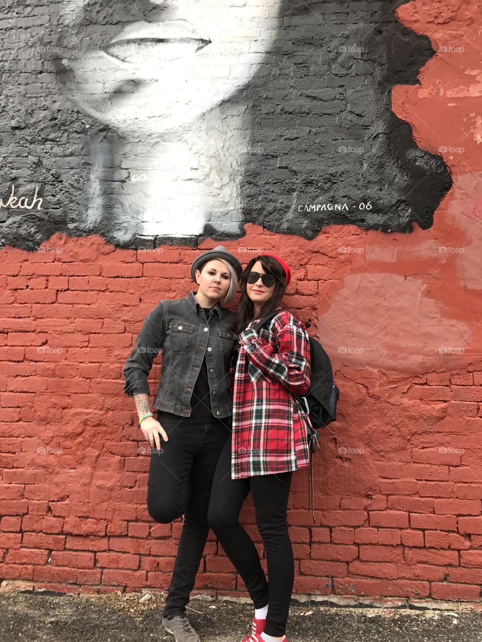 Two woman posing near the brick wall