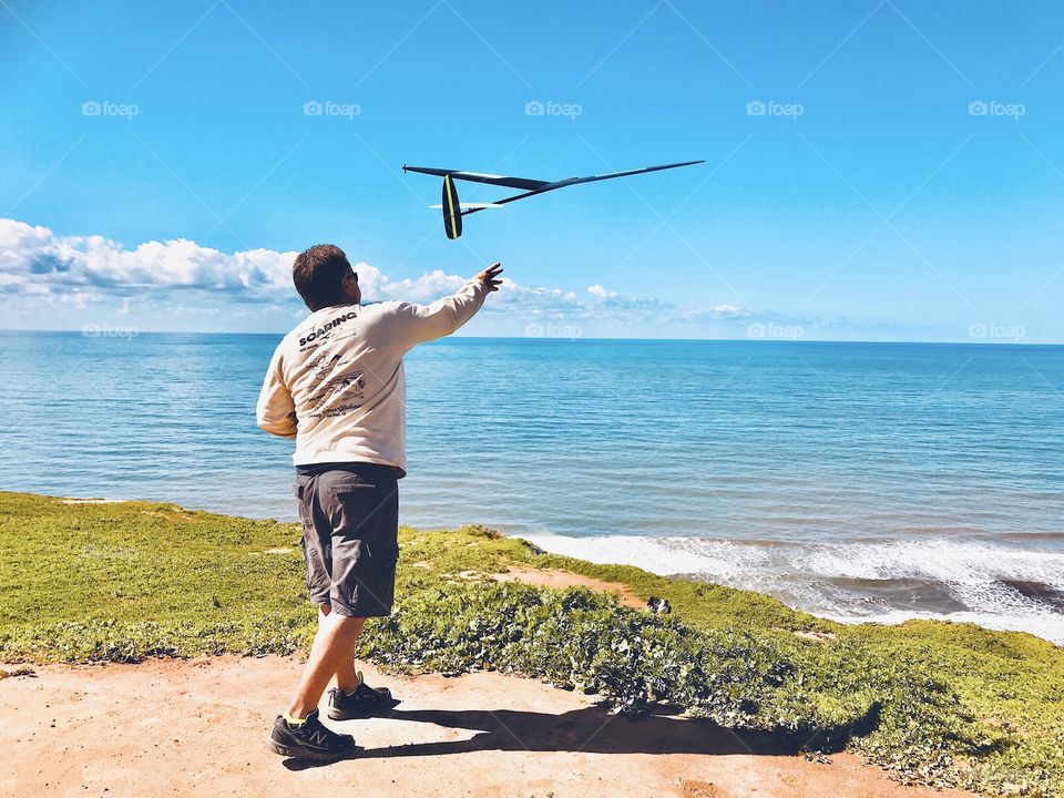A man stands on a cliff and throws his remote controlled glider into the wind. No motor just soars on the air and the remote moves the wing flaps and tail