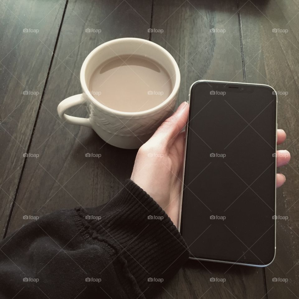Favorite coffee mug - woman holding cell phone while having a cup of coffee 