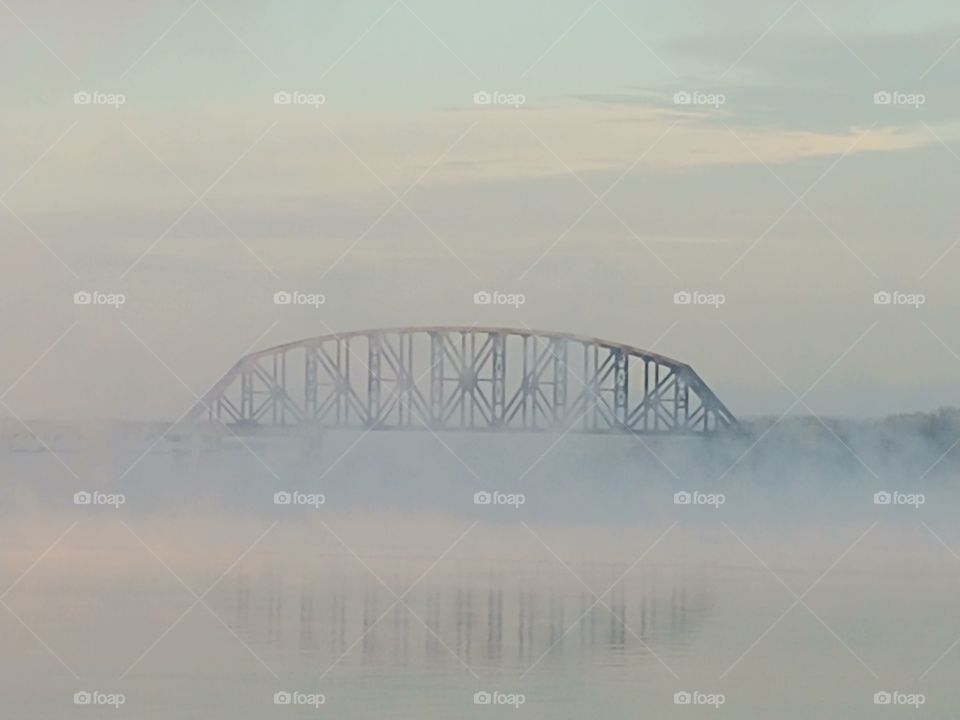 Morning fog coming off the Ohio River surrounds a railroad bridge .