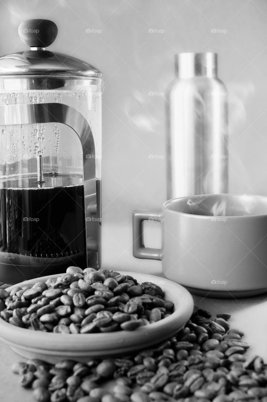 Closeup shot of coffee mug with steam and coffee beans spilled around in b&w