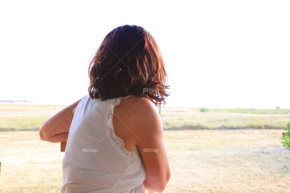 Woman with brown hair sitting in an open window looking out 